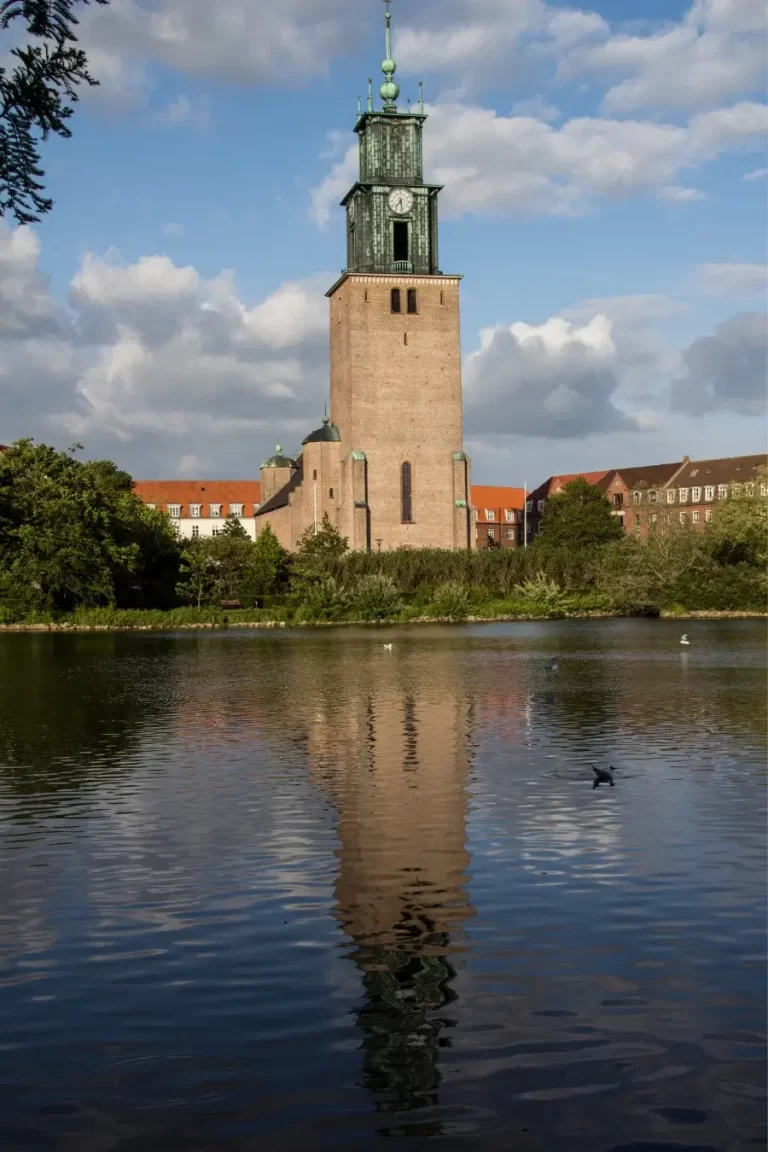 Iglesia de ladrillo con torre verde reflejada en un estanque de Aalborg, en Dinamarca