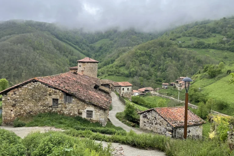 Casas de piedra de Bandujo con la torre medieval al fondo, entre montes verdes, en Proaza (Asturias)