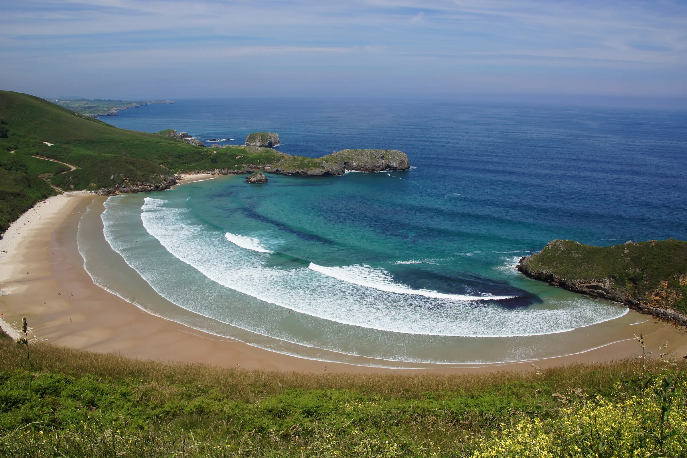 Playa de Torimbia, en Llanes, vista desde lo alto: arenal en forma de concha entre prados y cabos verdes