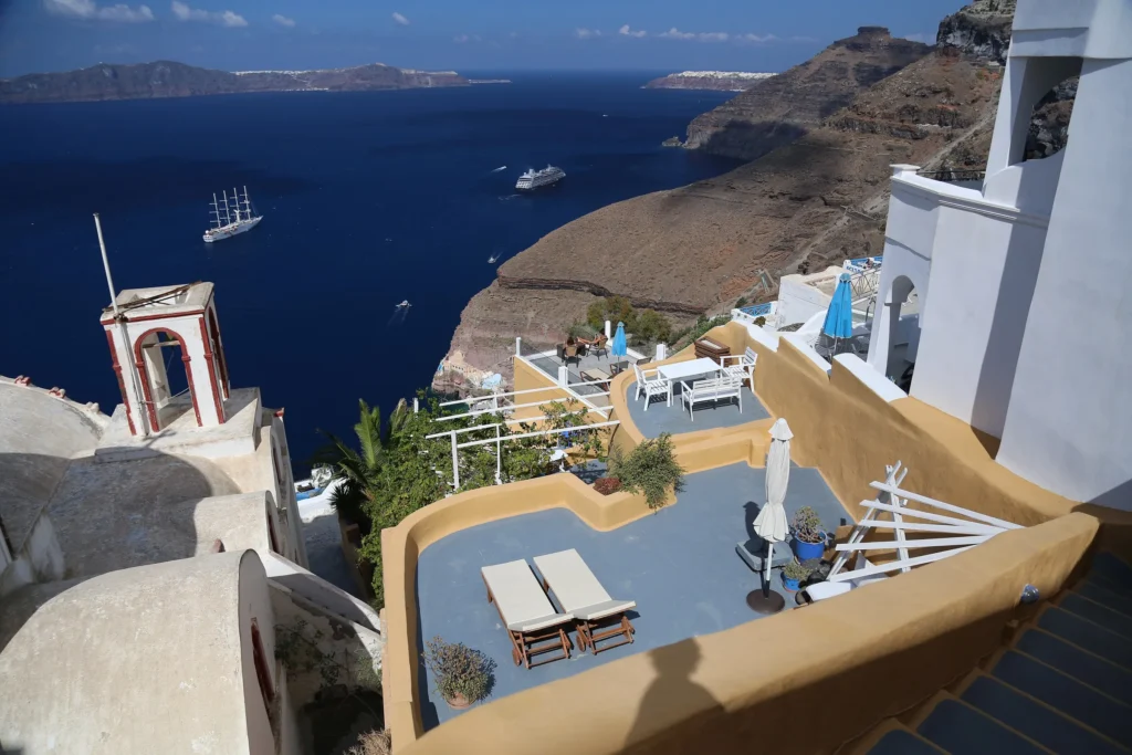 Terraza de un alojamiento de Fira con tumbonas sobre la caldera de Santorini, con barcos fondeados en el agua
