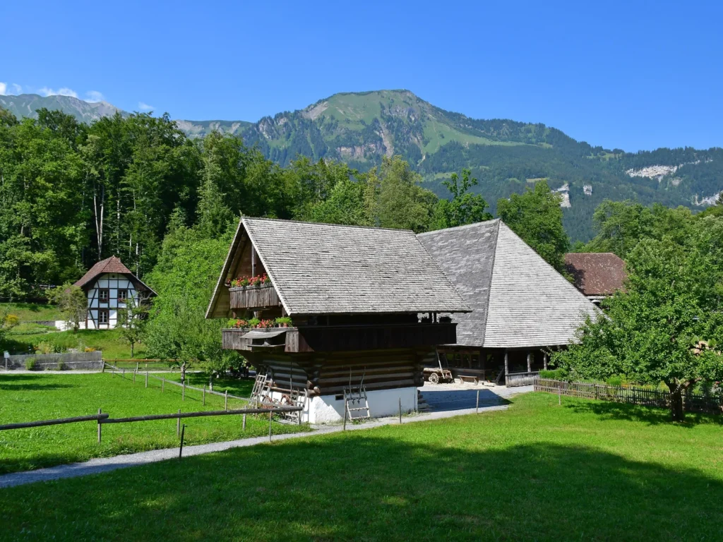 Una granja de madera del Museo Suizo al Aire Libre de Ballenberg, con prados y montañas detrás