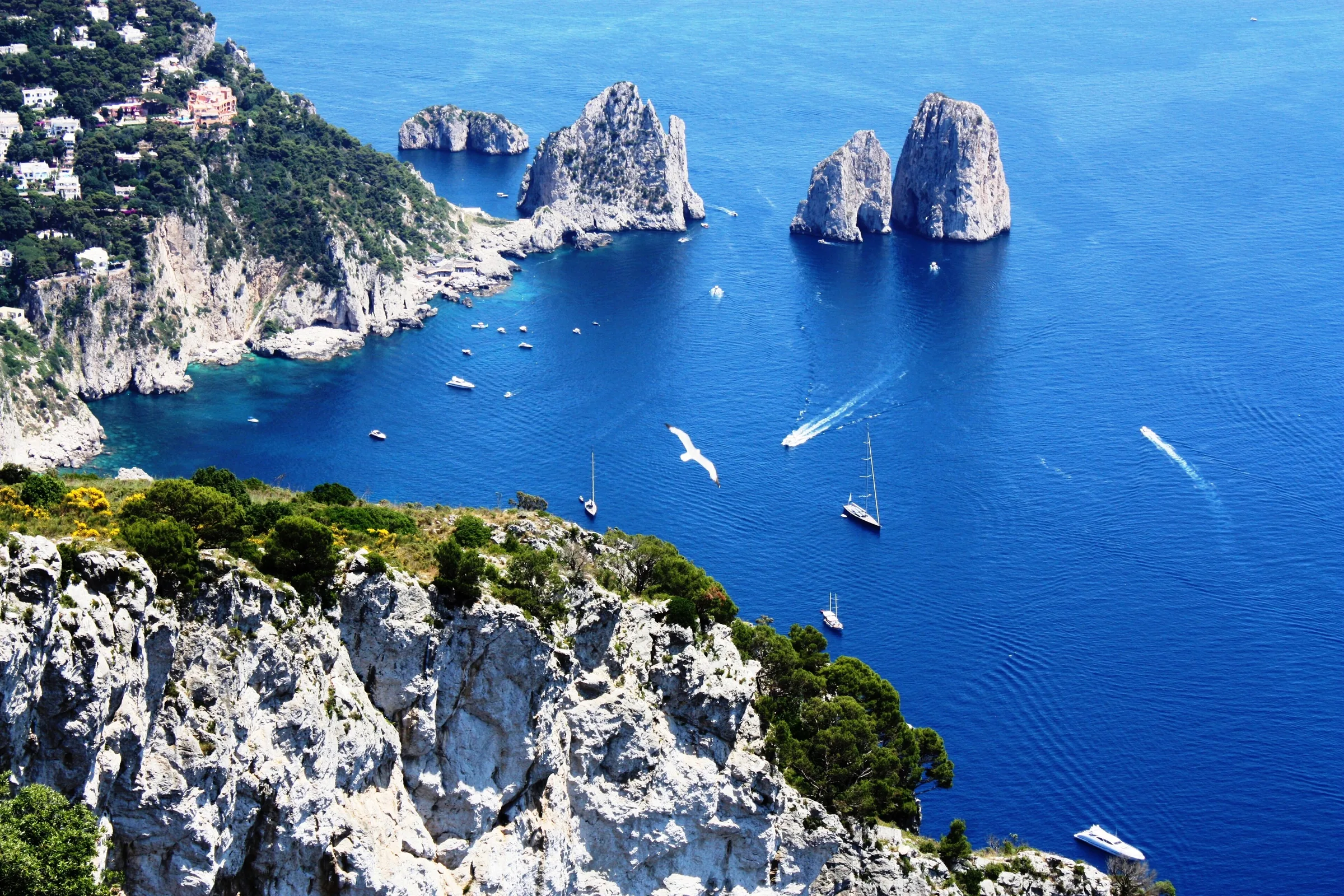 Los Faraglioni de Capri en un mar azul intenso, con barcos