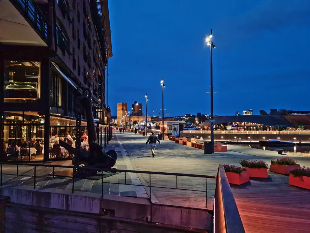 Paseo junto al agua en Aker Brygge al anochecer, con terrazas iluminadas