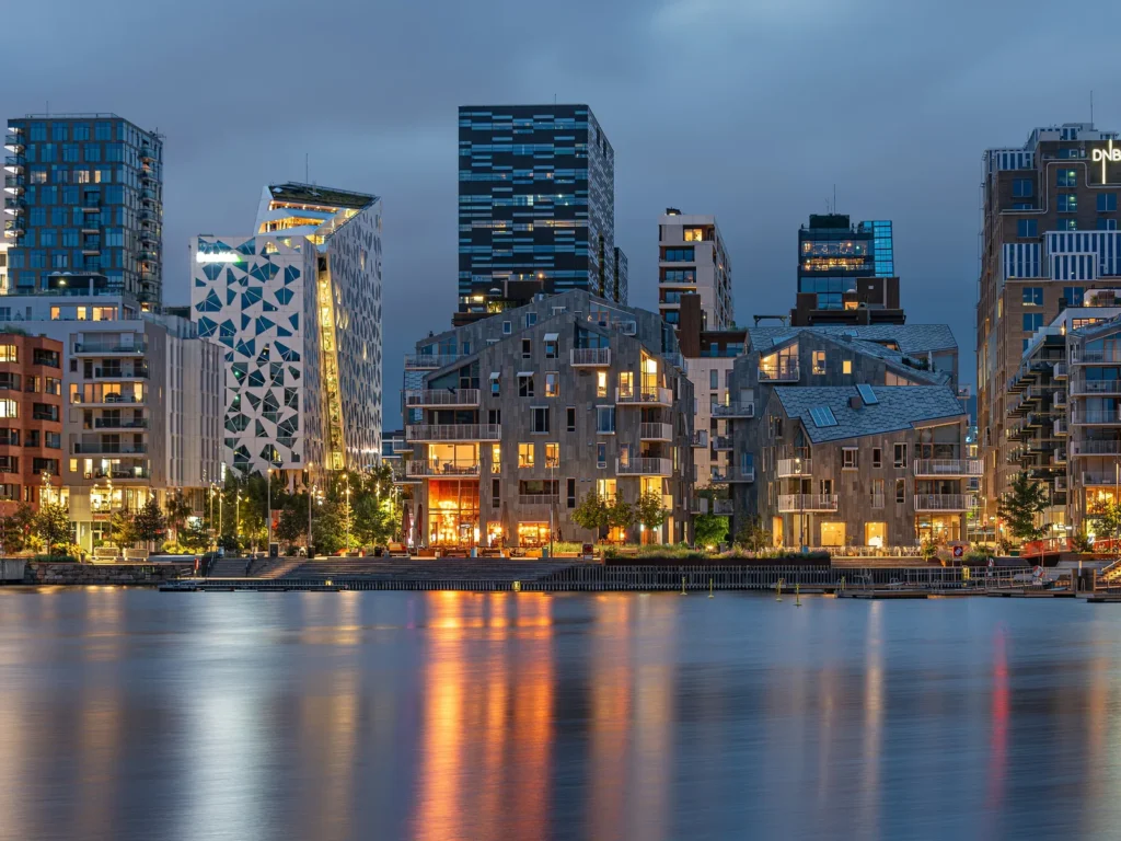 Edificios altos de Bjørvika iluminados al anochecer, reflejados en el agua