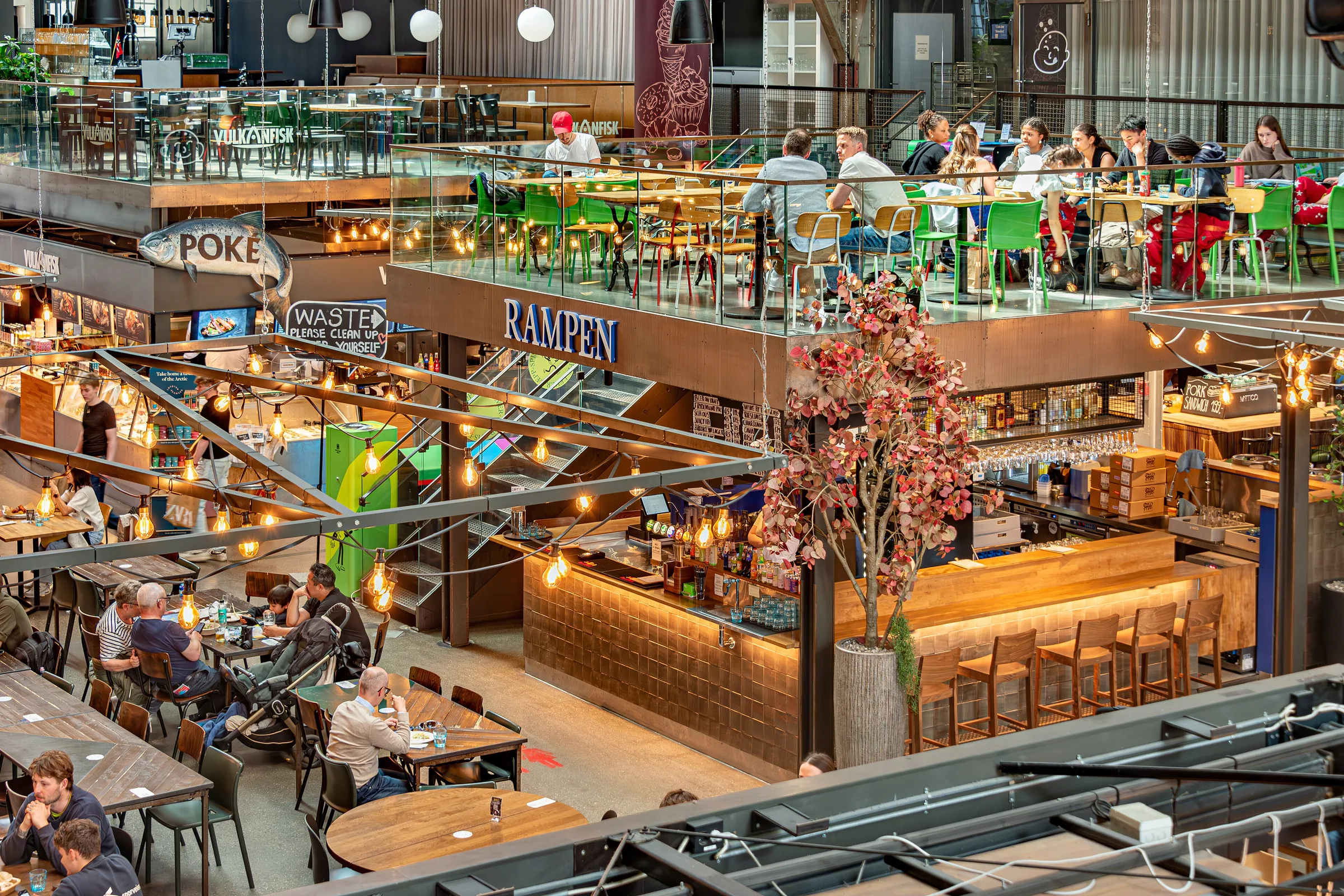 Interior de Mathallen, el mercado gastronómico de Oslo, visto desde la galería, con puestos y mesas