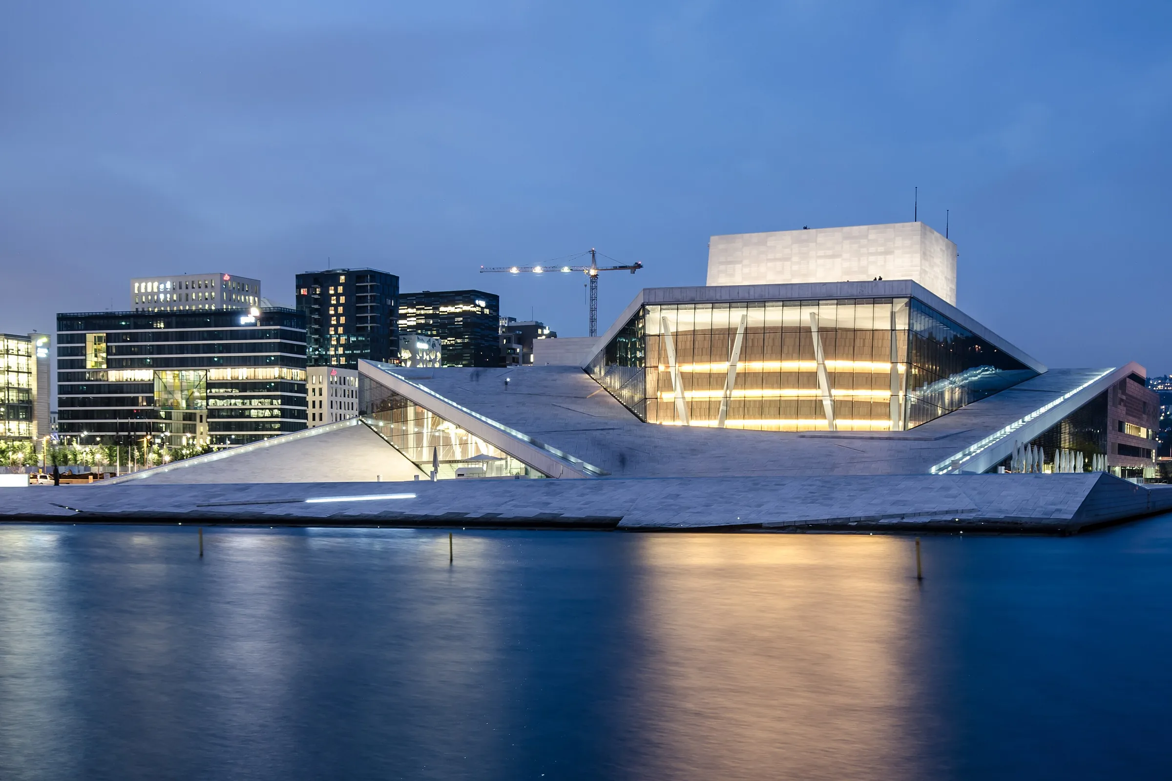 La Ópera de Oslo iluminada al anochecer, reflejada en el agua del fiordo